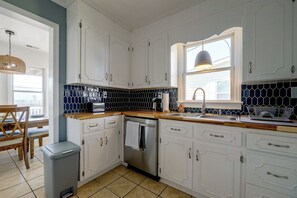 A kitchen with white cabinets, a black tiled backsplash, a wooden countertop, and a window with a hanging light fixture. - Salty Chateau Home w/ Ocean Views, Surf City (Surf City)