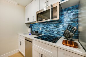 Eine moderne Küche mit weißen Schränken, einer Edelstahl-Mikrowelle, einer Glaskochplatte und einer blauen Mosaik-Spritzschutzwand.
