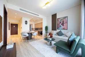 A modern living room with a green sofa, a coffee table, and a dining area with chairs. - Bloomfields-1BR-Saadiyat Beach Residence (Abu Dhabi)