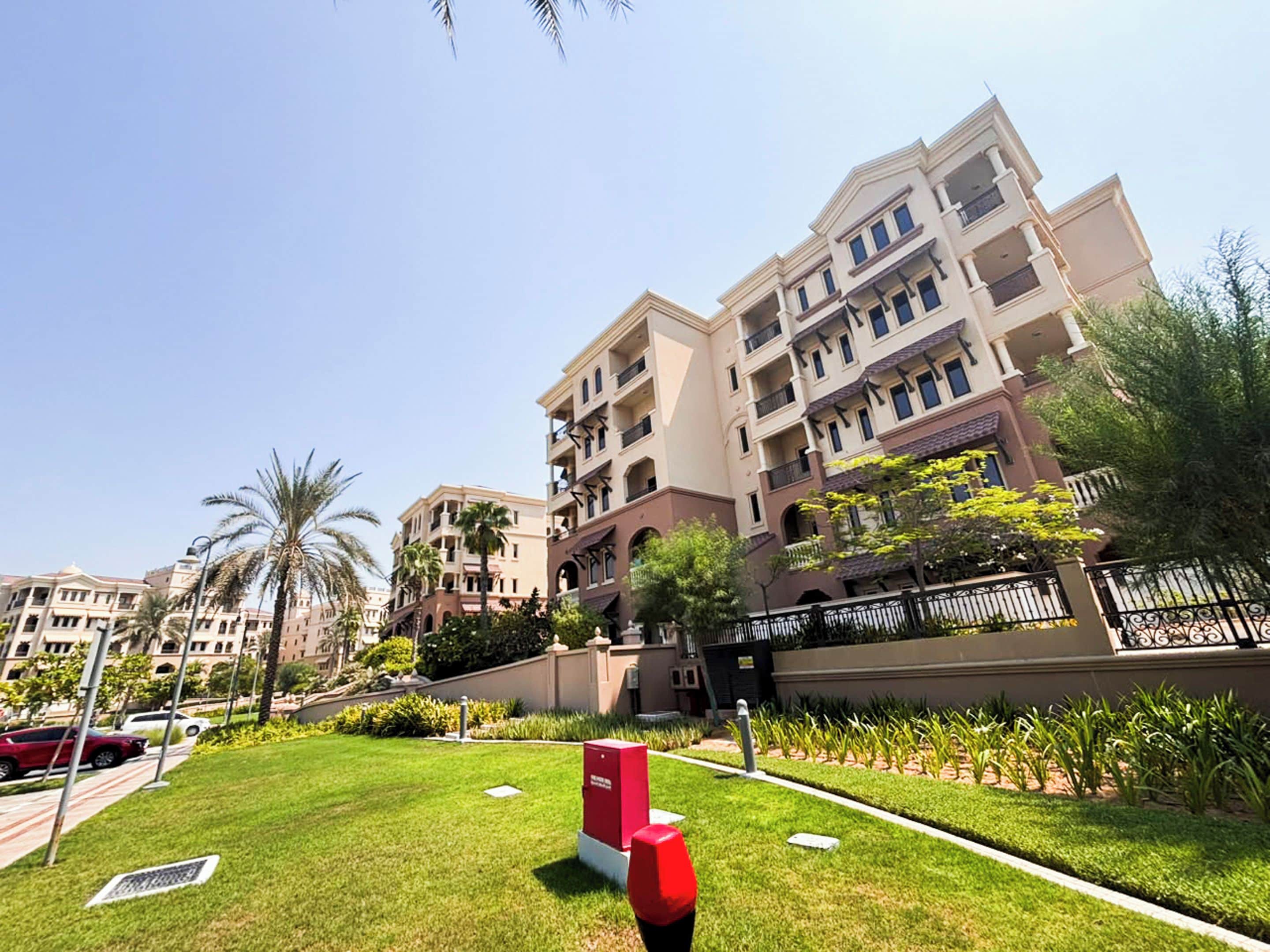 A multi-story residential building with balconies, a well-maintained lawn, and a gated entrance.