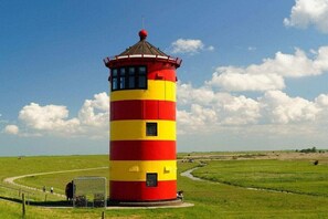 A cylindrical lighthouse with alternating red and yellow stripes, a small entrance, and a clear sky in the background. - Holiday apartment in Emden with swimming pool (Emden)