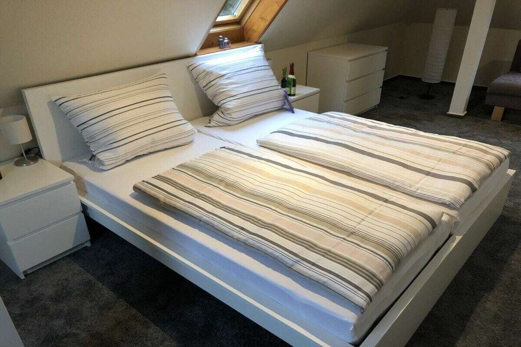 A bedroom with a bed, two bedside tables, a nightstand, a window, and a small shelf with a bottle.