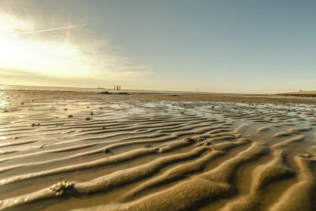 Une plage avec des motifs dessinés dans le sable humide et des bâtiments qui se dessinent à l’horizon.