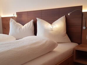 Ein ordentlich bezogenes Bett mit weißer Bettwäsche und Kissen, ein hölzerner Kopfteil und ein Nachttisch mit einer Lampe.