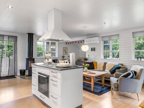 Une cuisine moderne dotée d’un îlot central, d’un coin repas avec un canapé et une table, et de grandes fenêtres qui laissent entrer la lumière naturelle.