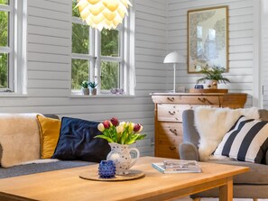 A room with a wooden table, a sofa with cushions, a vase with flowers, and a dresser with a lamp. - "Bennek" - 500m from the sea by Interhome (Egernsund)
