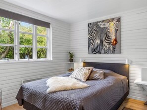 Ein Schlafzimmer mit einem großen Bett, einem Zebra-Gemälde, einem Fenster mit Blick auf Bäume und einem weißen Kopfteil.