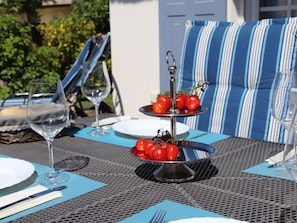 An outdoor dining setup with a metal table, two-tiered serving tray with tomatoes, wine glasses, and a striped cushion in the background. - Holiday Home in Glowe With Sauna (Glowe)