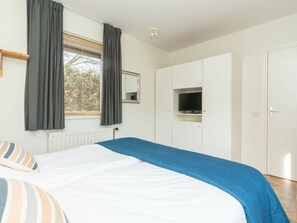A bedroom with a bed, a wardrobe, a television, and a window with curtains. - Holiday Home With 2 Bedrooms (Burgh-Haamstede)