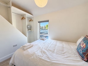 Une chambre à coucher avec un lit, une fenêtre, un ventilateur et une vue sur les bâtiments à l’extérieur.