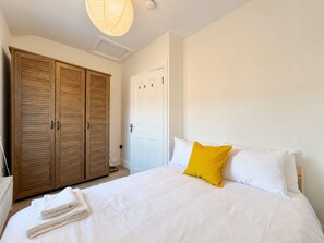 Ein Schlafzimmer mit einem Bett, weißer Bettwäsche, einem gelben Kissen, einem Holzschrank und einer weißen Tür.