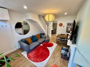 Un salon moderne avec un canapé gris, un tapis rouge et un escalier menant à un autre niveau.