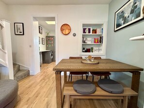 Ein Essbereich mit Holztisch und Bank, einer Uhr an der Wand und einem Bücherregal mit Büchern und Dekoration.