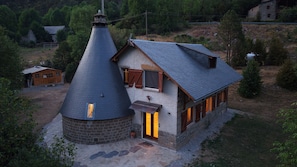 Una casa de pedra amb teulada cònica i un annex rectangular, en un paisatge rural.