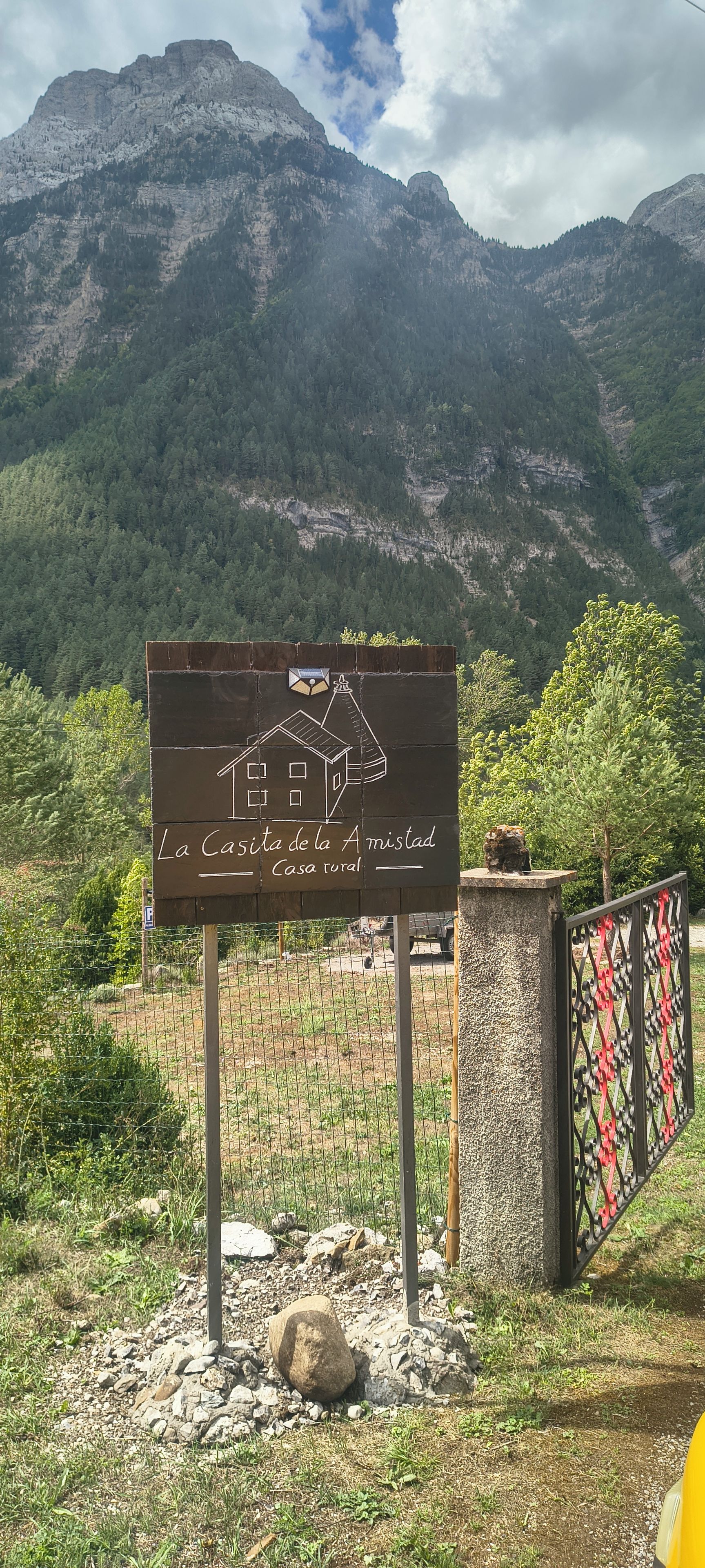 Schild für 'La Casa de la Amistad' mit Bergelandschaft im Hintergrund.