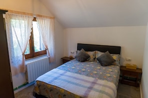 A bedroom with a bed, a window with curtains, a radiator, and a bedside table with a lamp.