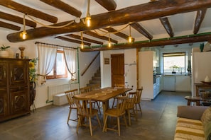 A spacious dining area with a wooden table and chairs, a kitchen in the background, and a staircase leading to another level.