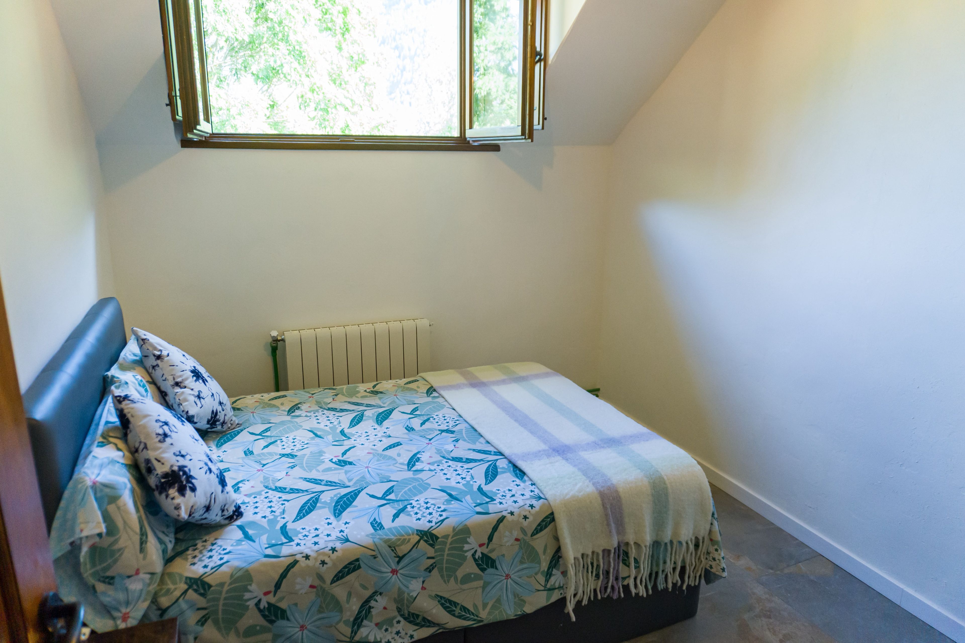 A small, single-bed room with a window, a radiator, and a bed with floral bedding.