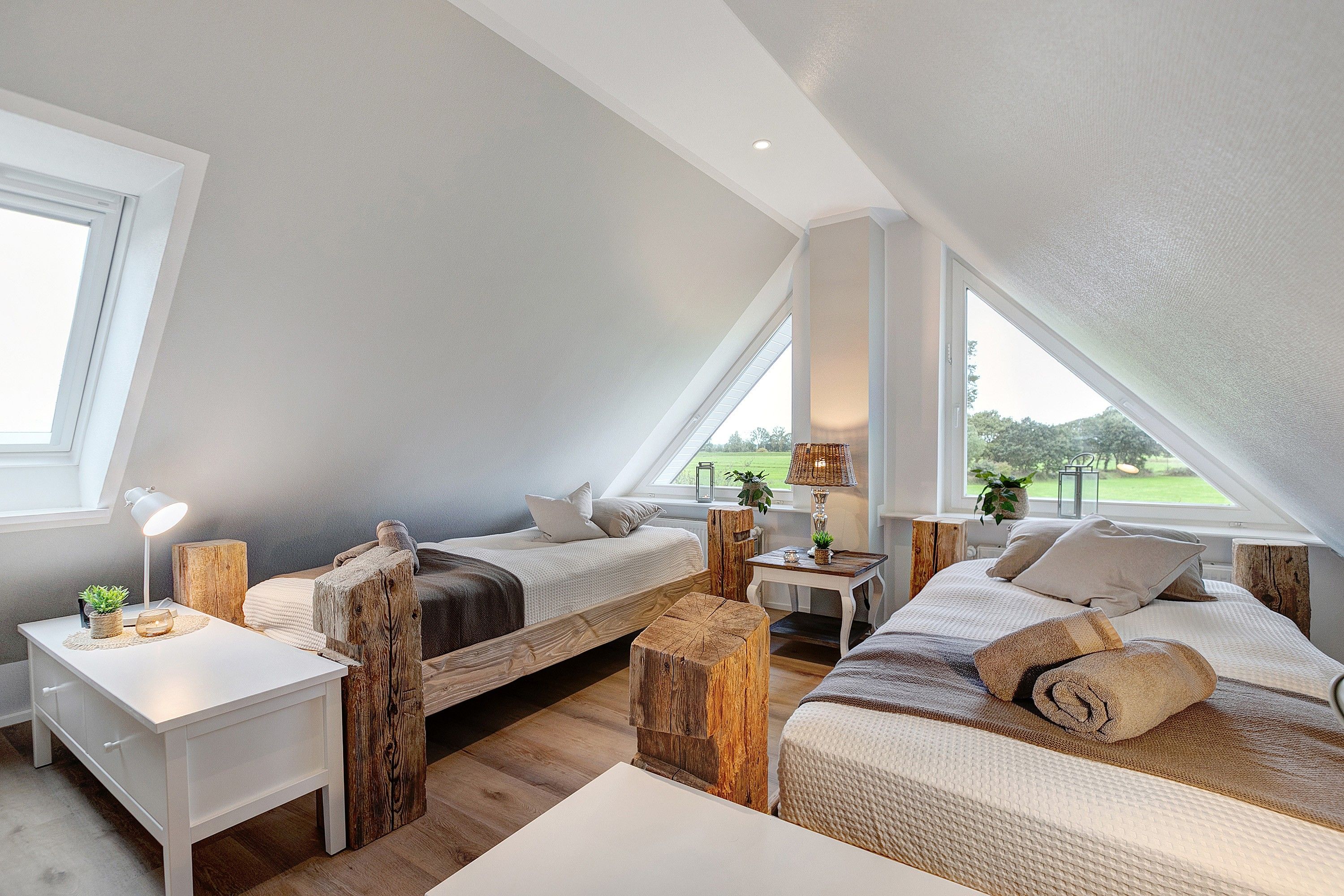 A cozy attic bedroom with two beds, a small table, and a view of the outdoors.