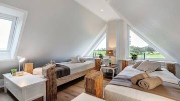 A cozy attic bedroom with two beds, a small table, and a view of the outdoors.