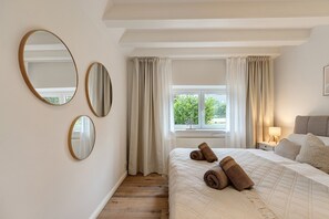 A bedroom with a bed, two mirrors, a window with curtains, and a bedside table with a lamp.
