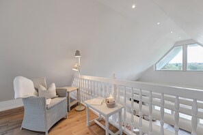 A room with a high ceiling, a white railing, a wicker sofa, a floor lamp, and a table with a candle.