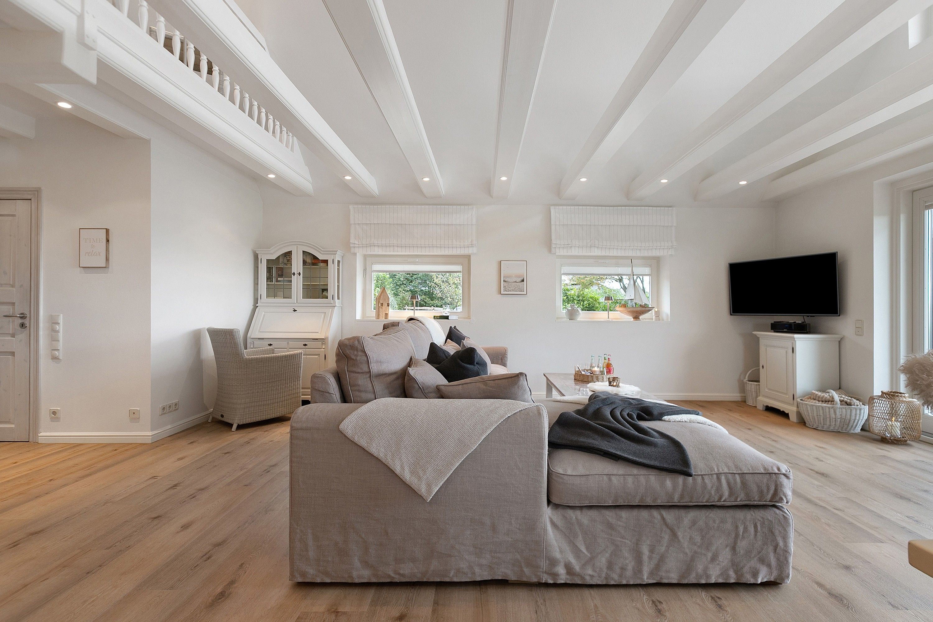 A spacious living room with a large sofa, a television, and a window with a view of greenery.