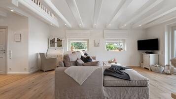 A spacious living room with a large sofa, a television, and a window with a view of greenery.