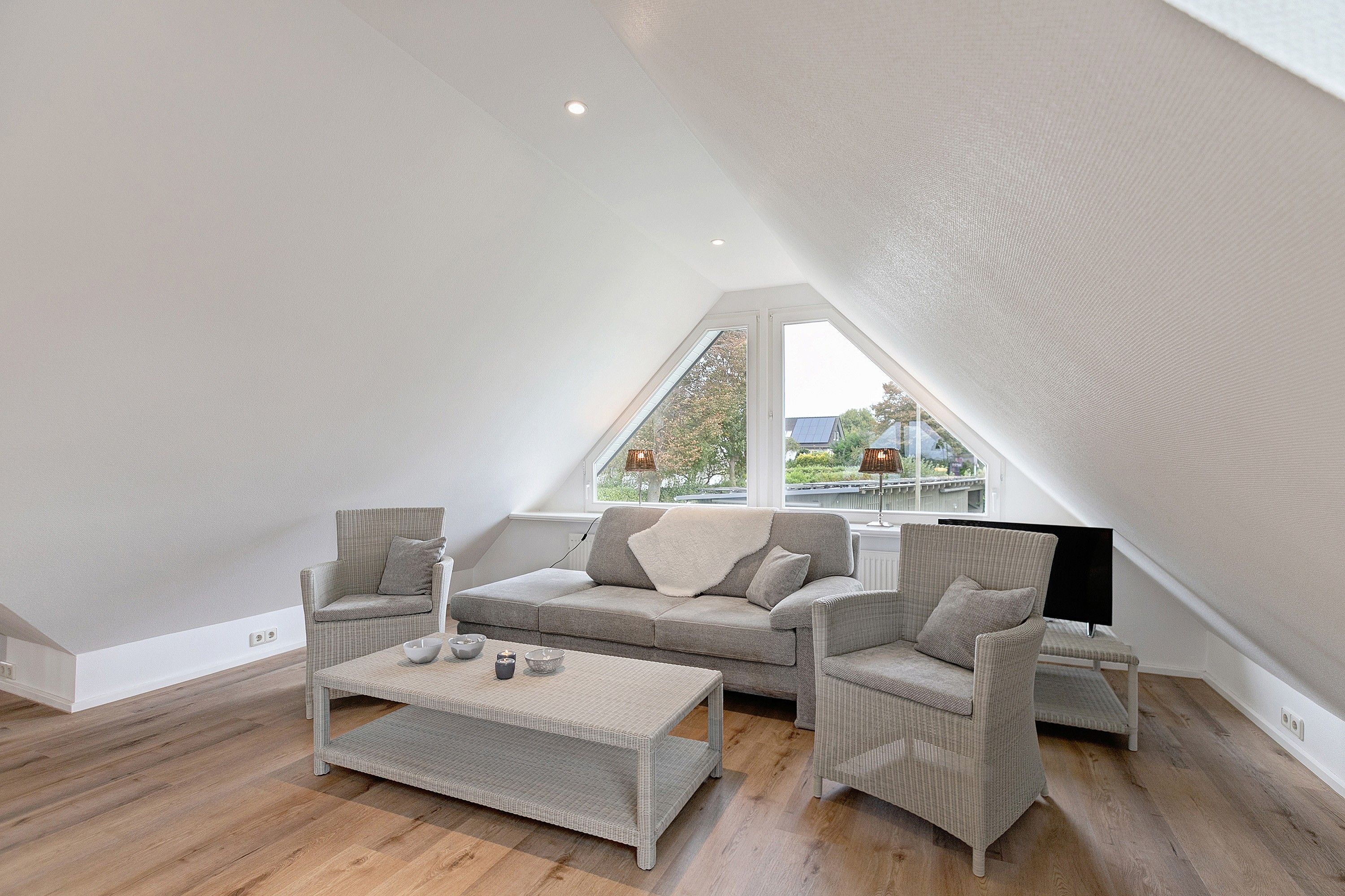 Een moderne loft slaapkamer met schuine plafonds, een groot raam en een gezellige zithoek met een bank en fauteuils.