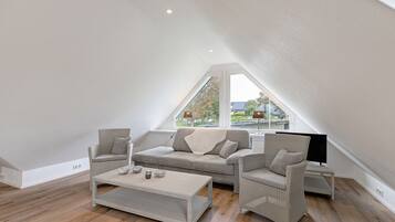 Een moderne loft slaapkamer met schuine plafonds, een groot raam en een gezellige zithoek met een bank en fauteuils.