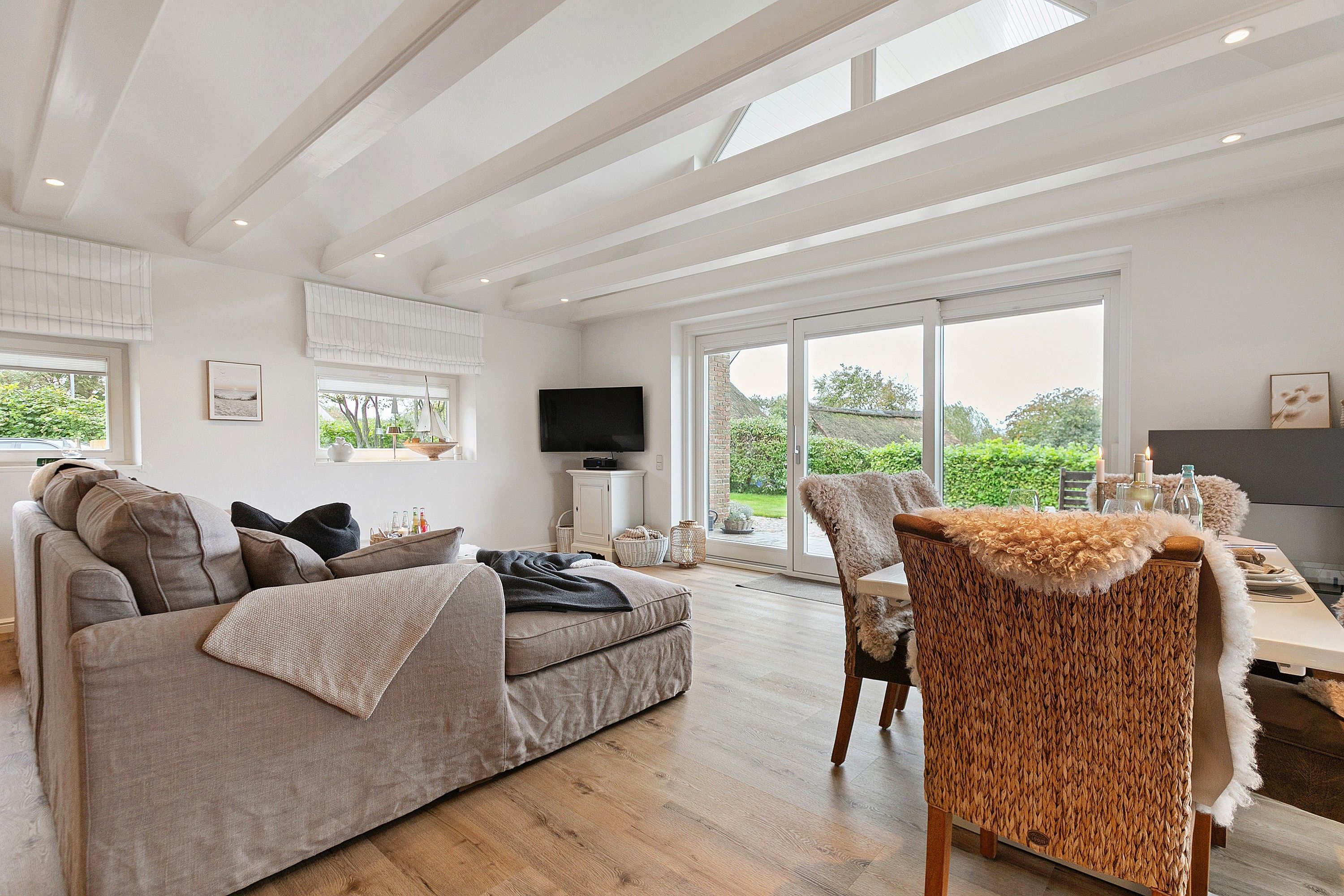 A spacious living room with a sofa, a television, and a large window offering a view of the outdoors.