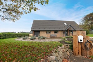 A house with a sloped roof, a stone pathway leading to the entrance, and a wooden fence with a charging station.