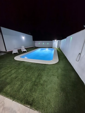 Ein Schwimmbecken mit Kunstrasen, umgeben von weißen Wänden und einem weißen Zaun.