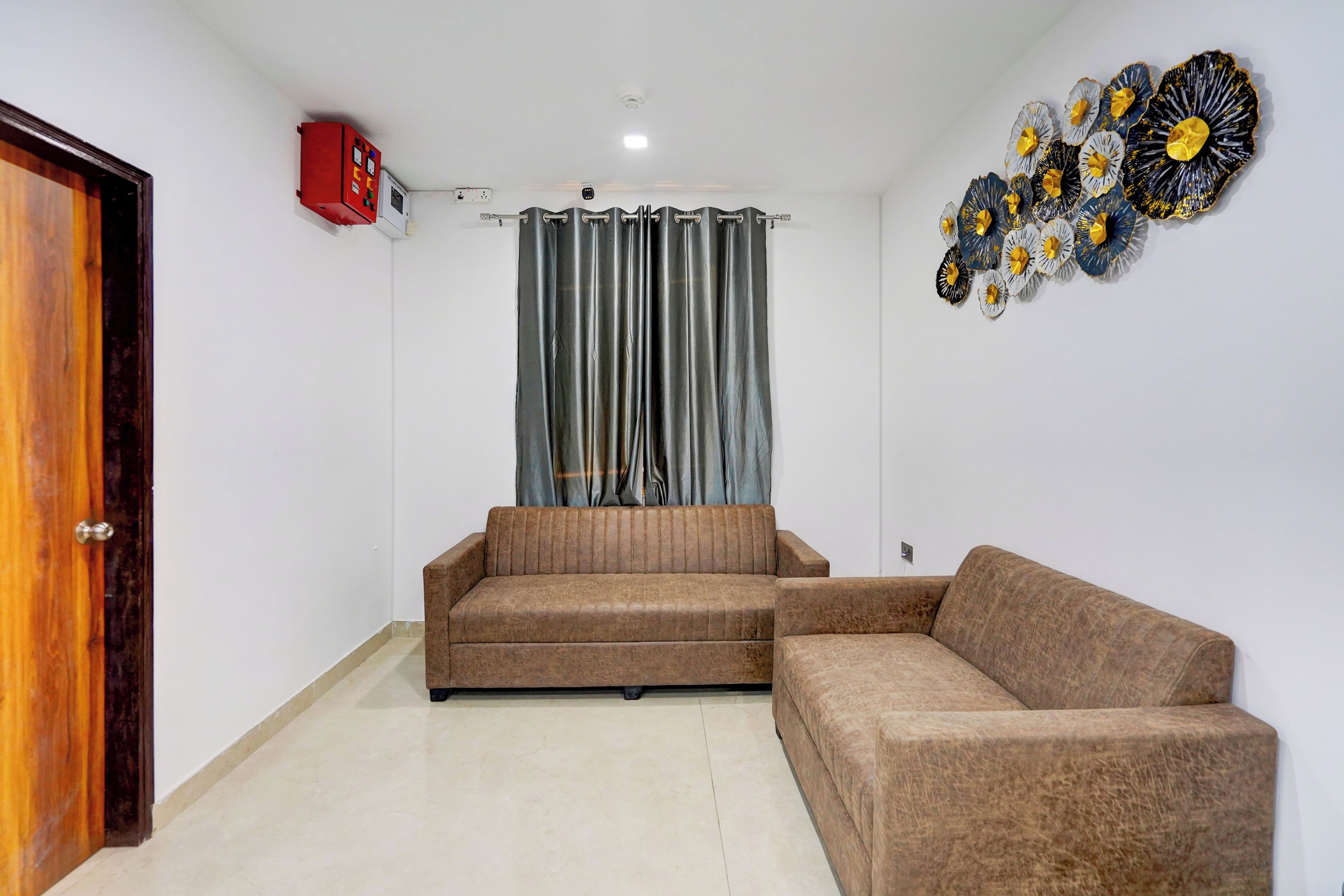 A living room with a brown sofa, a grey curtain, and a wall decoration.