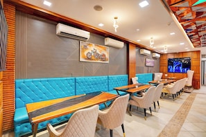 Interior de restaurante con asientos acolchados azules, mesas de madera y unidades de aire acondicionado en las paredes.