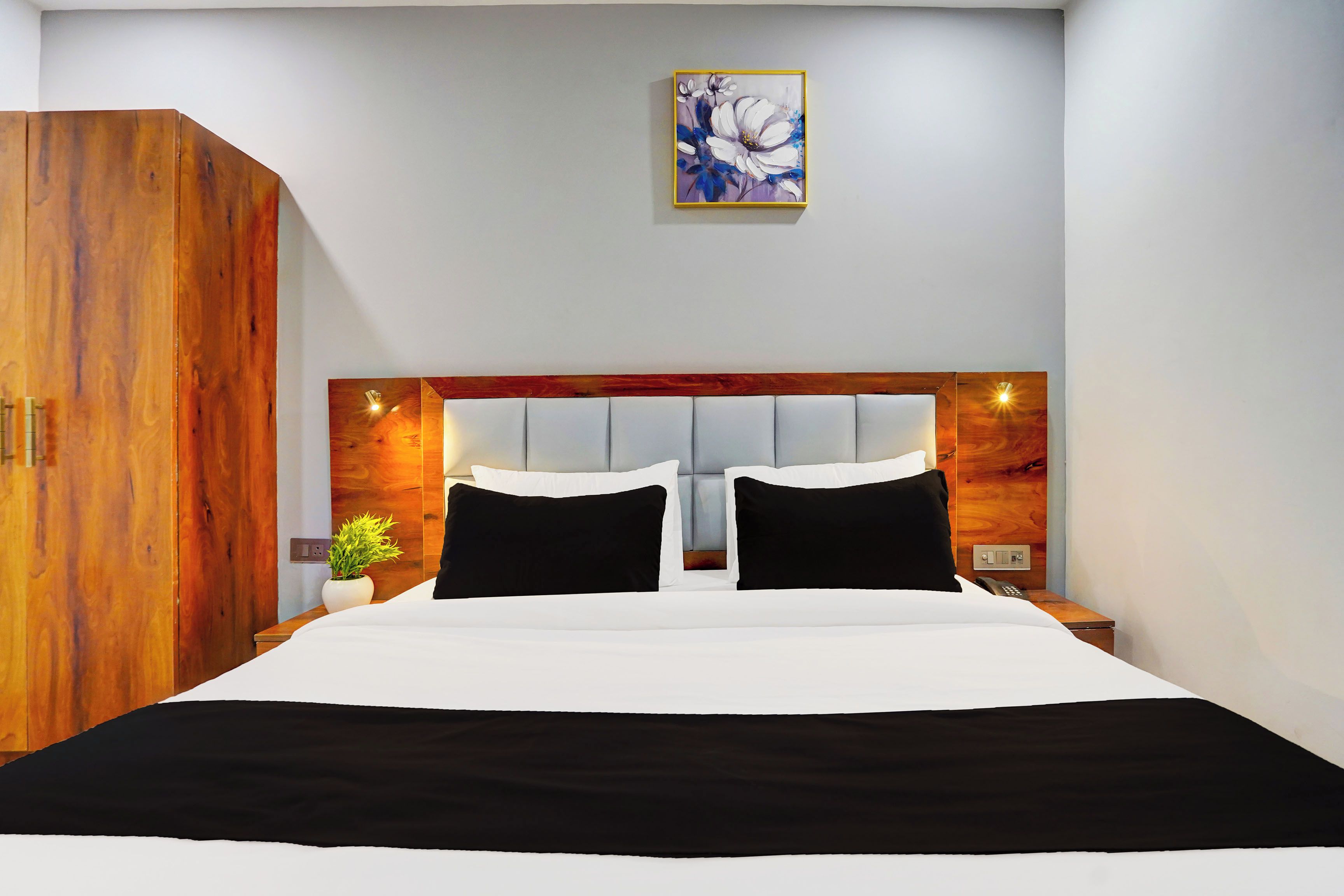 Quarto de hotel com uma cama grande, guarda-roupa de madeira, mesa de cabeceira com abajur e um quadro na parede.