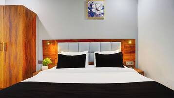 Quarto de hotel com uma cama grande, guarda-roupa de madeira, mesa de cabeceira com abajur e um quadro na parede.