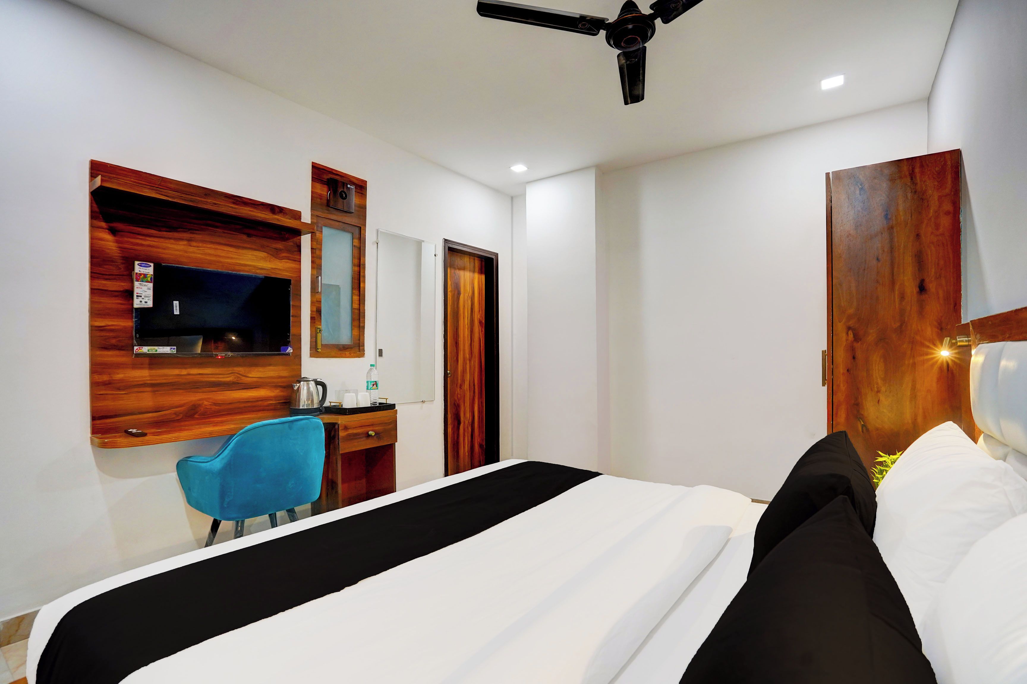 Ein Hotelzimmer mit einem Bett, einem Schreibtisch mit Stuhl, einem Holzschrank und einem Deckenventilator.