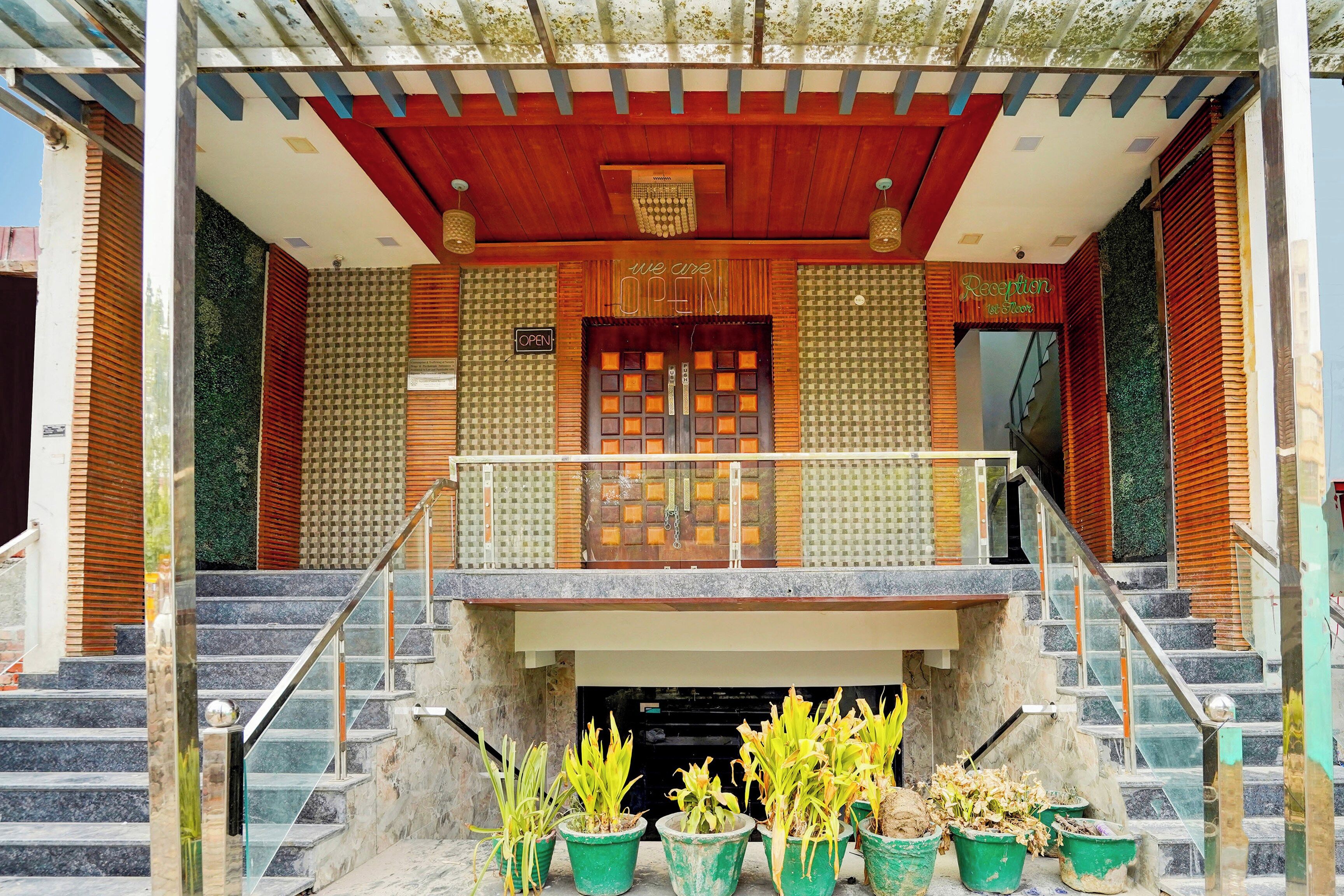 A hotel entrance with a reception desk, a staircase, and potted plants.