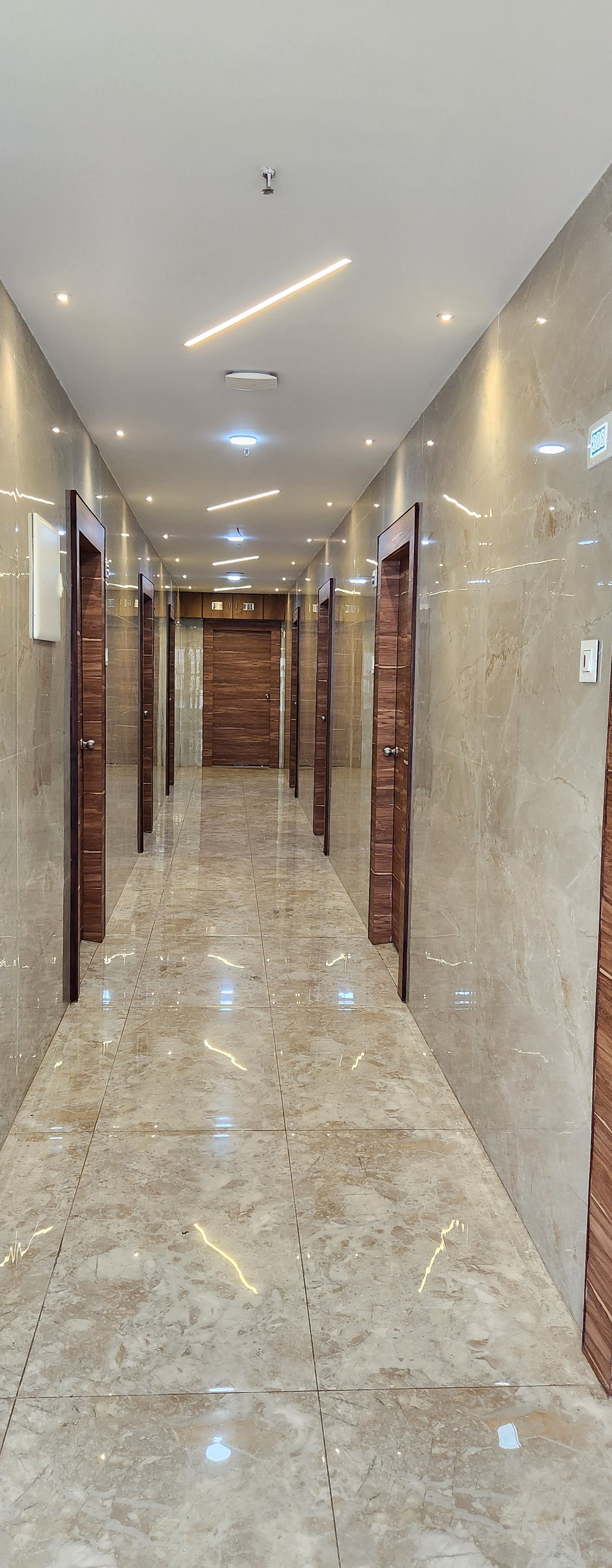 A corridor with marble flooring, wooden doors, and recessed lighting.