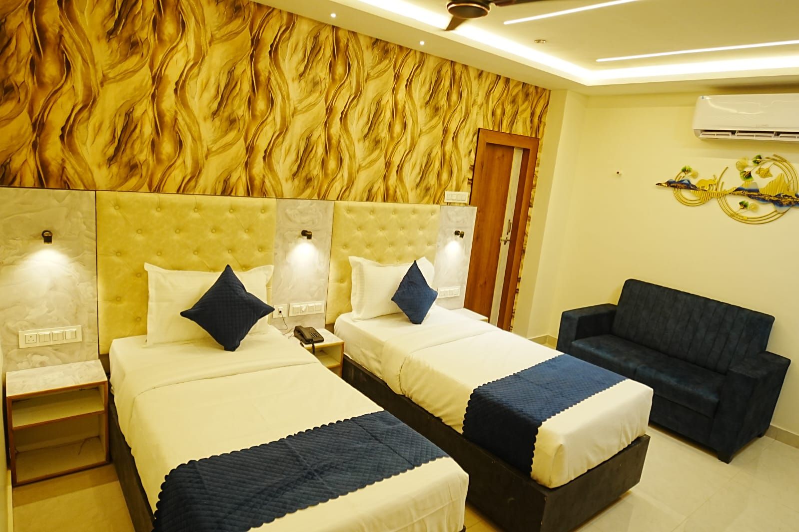 Habitación de hotel con dos camas, un sofá y un muro decorativo.