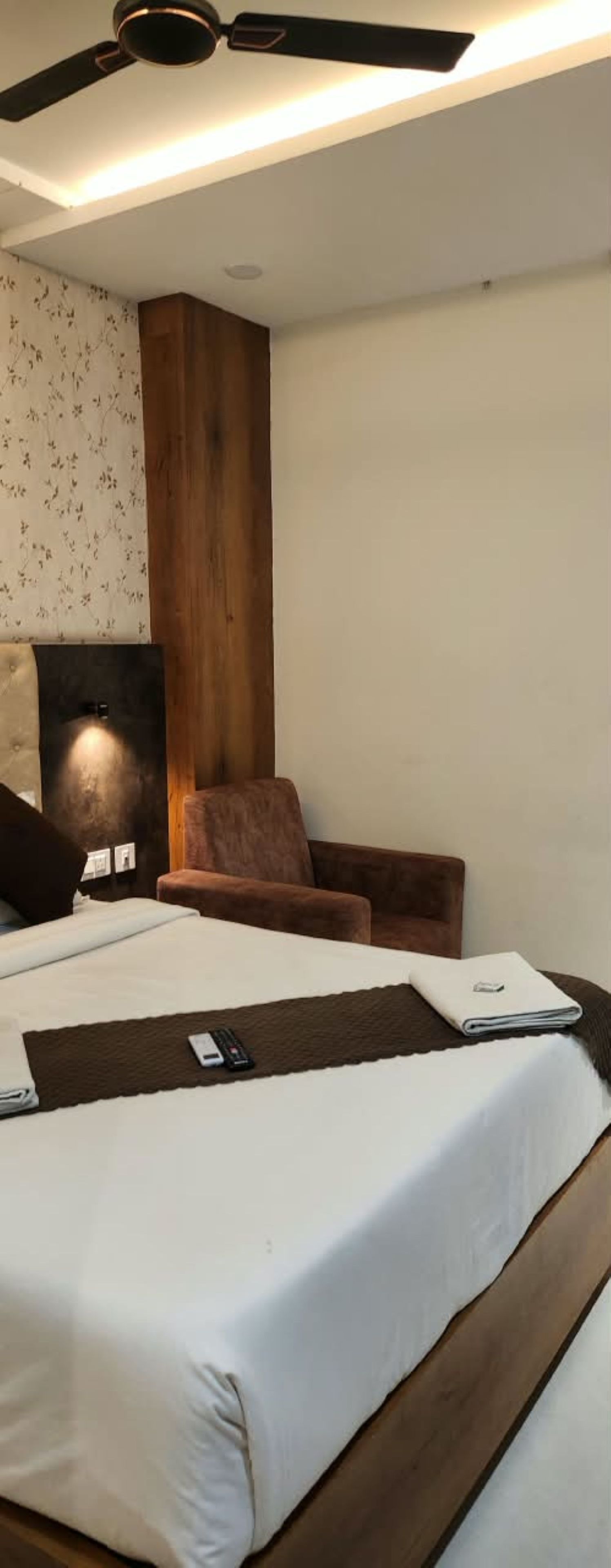 A hotel room with a bed, a chair, a desk, and a ceiling fan.