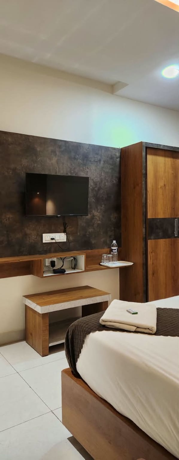 A modern bedroom with a bed, a TV mounted on a textured wall, a wooden bedside table, and a wardrobe. - Hotel Moon Light (Vijayawada)
