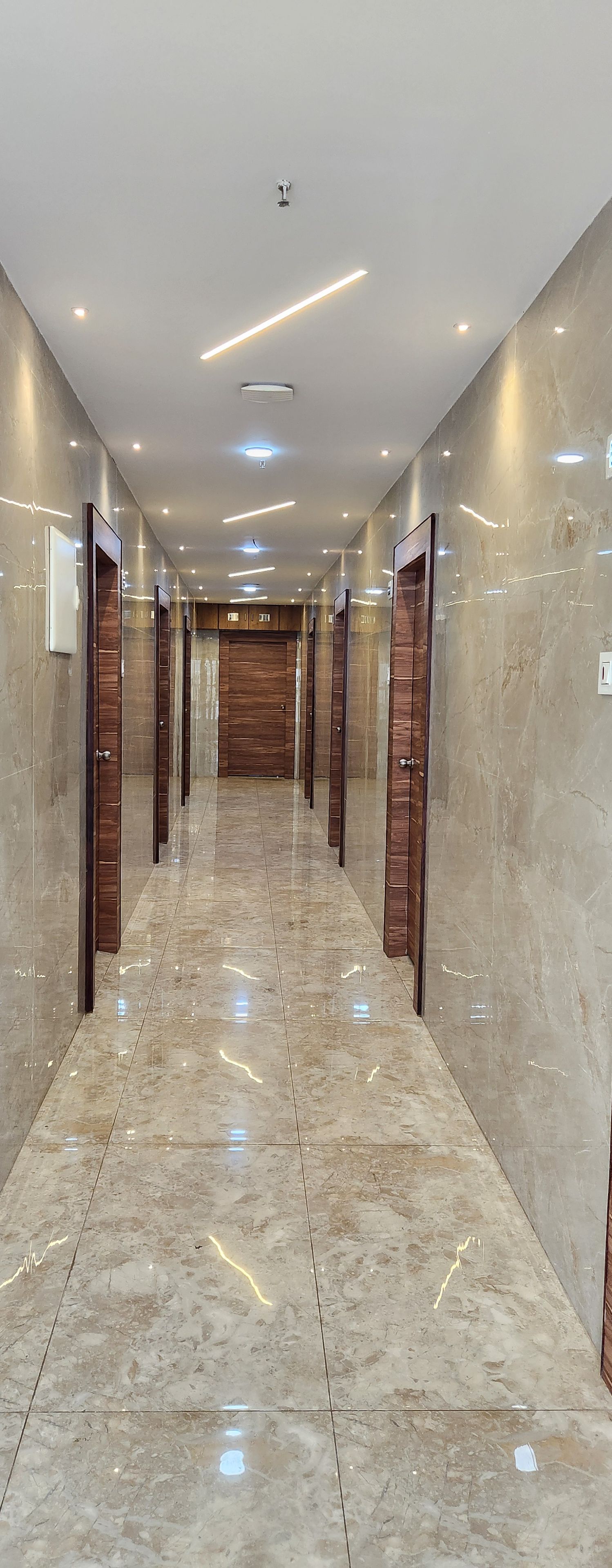 A hallway with marble flooring, wooden doors, and recessed lighting.