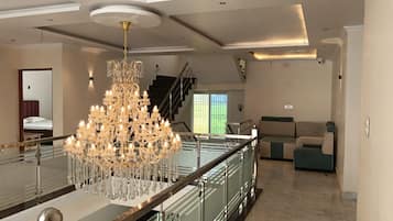 A spacious living area with a grand chandelier, a staircase, and a view of a green outdoor area.