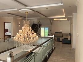 A spacious living area with a grand chandelier, a staircase, and a view of a green outdoor area.