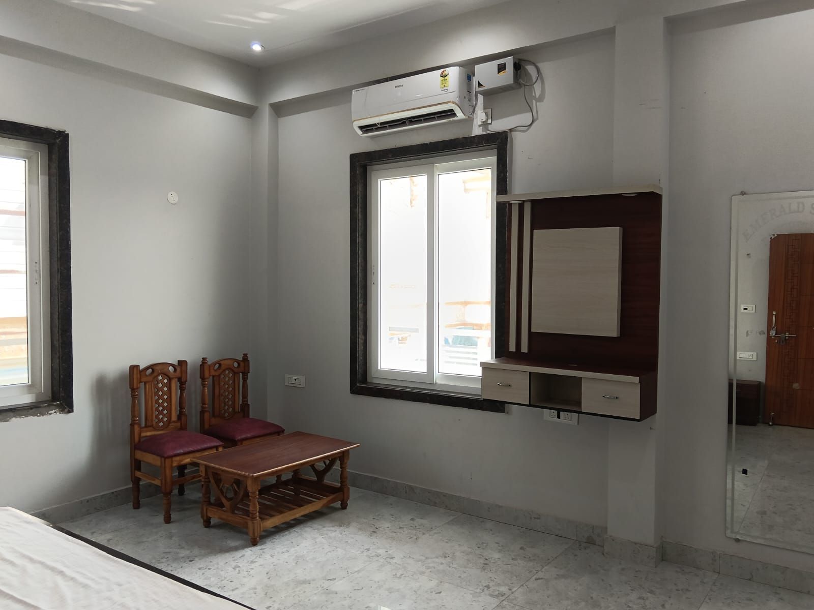 Una habitación con cama, una mesa de madera, dos sillas, una ventana con vistas, un equipo de aire acondicionado y una puerta.
