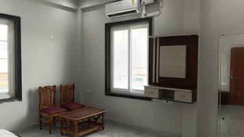 Una habitación con cama, una mesa de madera, dos sillas, una ventana con vistas, un equipo de aire acondicionado y una puerta.