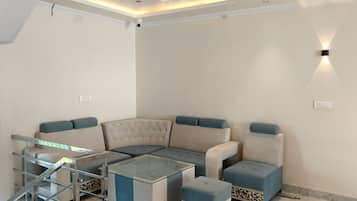 Una sala de estar moderna con un sofá seccional, una mesa de centro de vidrio y un pequeño otoman.