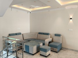 Uma sala de estar moderna com um sofá seccional, uma mesa de centro de vidro e um pequeno banquinho.